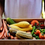 Young man at the door delivering Farm Share box full of fresh vegetables