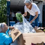 Pam, left, receives help from Iskam MәkhMәk-Haws volunteer Debbie during a mobile pantry distribution at a mobile home park in Willamina.