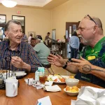 Richard, left, and Jimbo chat while eating lunch together at the Meals on Wheels dining room at Center 50+. In-person meal service resumed earlier this year after being postponed for three years during the pandemic.